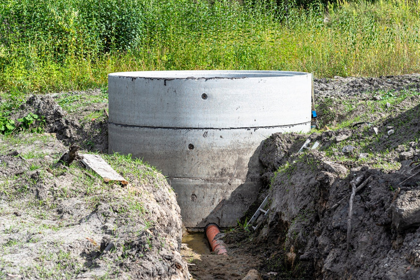 A concrete septic tank sunken into the ground, with a visible drain pipe